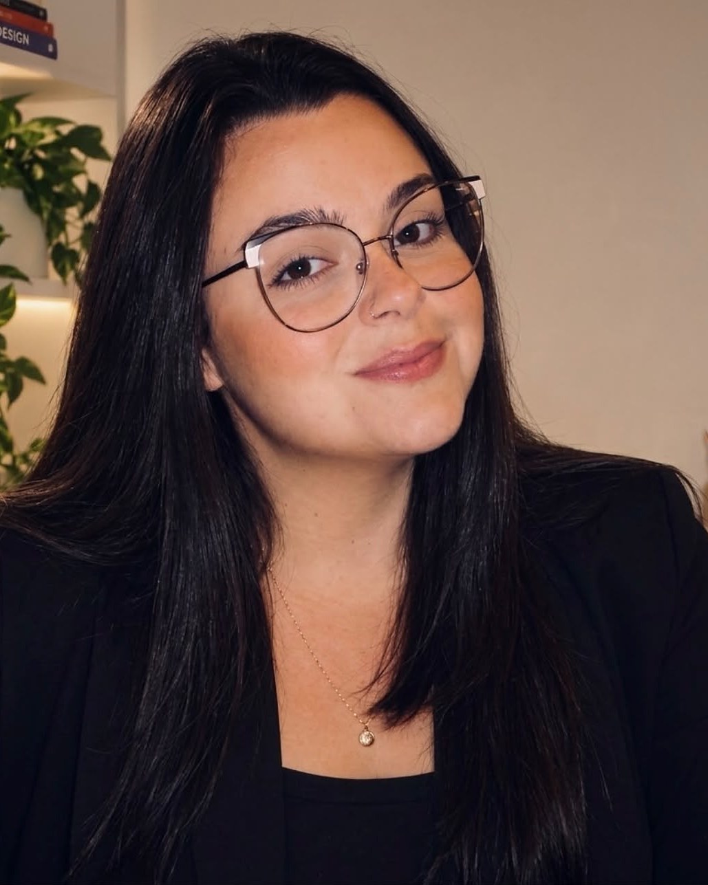 Victoria Valentini, psicóloga e neuropsicóloga, sorrindo em seu consultório, de óculos e blazer preto.